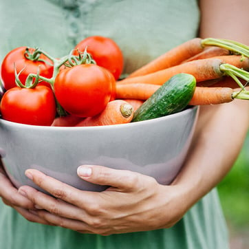 Frau trägt eine Schale mit frischem Gemüse, um damit gesund und ausgewogen zu kochen.